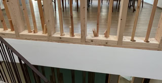 Foto der Treppengeländer, eines aus Metall für die Stufen und eines aus Holz und bis zur Decke für den Treppenabsatz.