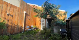 Outdoor area in front of the tiny house, behind the wooden fence. Small garden with a tree.