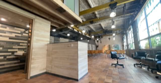 Photo de la grande salle du tiers-lieu au rez-de-chaussée après travaux. Le carrelage rappelle la brique au dehors tandis que les poutres nécessaires à l’activité industrielle participent à l’ambiance unique du lieu.